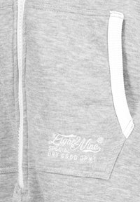 Grey zip-up sweatshirt with white zipper, side pocket, and embroidered logo detail in white text on left chest area. Soft, textured fabric.