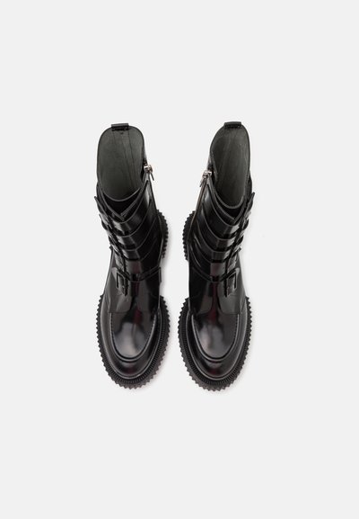 Black ankle boots with glossy patent leather, featuring three buckled straps, a rounded toe, and a textured rubber sole.