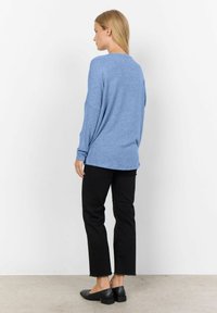 Blau gestrickter Pullover mit überschnittenen Schultern und langen Ärmeln, kombiniert mit schwarzen, cropped Hosen, von hinten auf einem neutralen Hintergrund präsentiert.