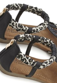 Zwarte platte sandalen met een gevlochten stoffen band in een zwart-wit patroon, ritssluiting en een getextureerde tan binnenzool.
