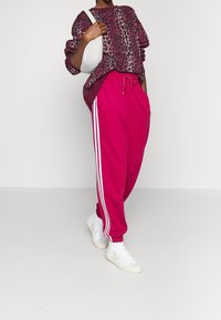 Leopardmönstrad sweatshirt i burgundy och rosa, kombinerad med rosa joggers med vita ränder och vita sneakers. Minimalistisk vit väska.