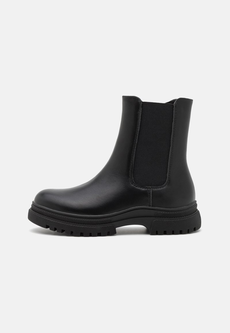 Bottine en cuir noir avec semelle épaisse crantée et empiècement latéral élastique sur fond gris uni.