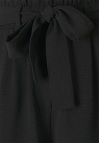 Tessuto nero in vita con un dettaglio di nodo. Texture morbida e finitura liscia. Il design presenta una banda elastica arricciata per un maggiore comfort.
