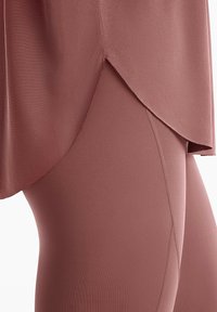 Leggings color rosa abbinati a un top asimmetrico coordinato. Il tessuto appare liscio, con cuciture visibili e un design pulito e minimalista.