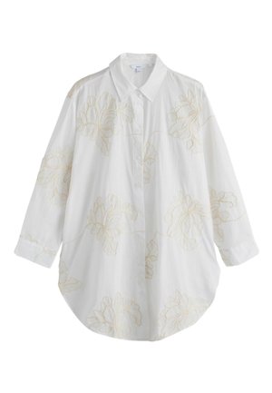 Camicia bianca a maniche lunghe con bottoni, ricamo floreale beige chiaro e colletto classico, mostrata su uno sfondo semplice.