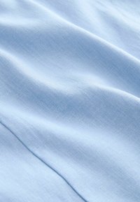 Helles blaues Gewebe mit einer glatten Textur, das leichte Falten und ein dezentes Webmuster aufweist, was ein sanftes, luftiges Erscheinungsbild vermittelt.