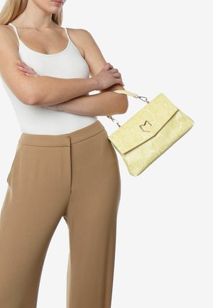 Geel met slangebont handtas met een omslagflap en gouden hardware, vastgehouden door een persoon die een witte tanktop en beige broek draagt.