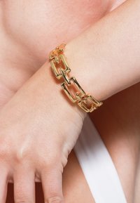 Bracciale in oro con maglie rettangolari interconnesse e finitura lucida, posato su un tono di pelle chiara.