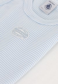 Light blue striped t-shirt with a crew neckline and a subtle white embroidered logo. Fabric appears soft and lightweight.