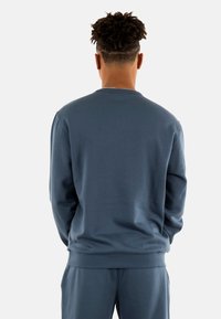 Sudadera azul con cuello redondo, puños y dobladillo acanalados, hecha de un material suave. Presenta una textura lisa y un corte relajado.