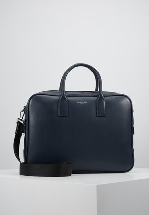 Malette en cuir noire avec deux poignées, une bandoulière amovible et un petit logo centré sur une surface blanche.