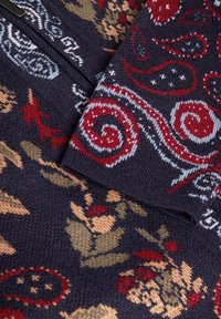 Gebreide trui met een marineblauwe achtergrond en bloemen- en paisleypatronen in rood, beige en blauw. Gestructureerde afwerking met een ritsluiting.