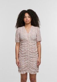 Robe rose à motifs floraux avec des manches courtes bouffantes, un décolleté en V et un détail froncé. Tissu léger avec un ourlet volanté.