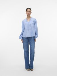 Lyseblå langermet skjorte med brodert bærestykke og slipsdetalj, kombinert med høyt liv og rette jeans samt grønne sandaler.