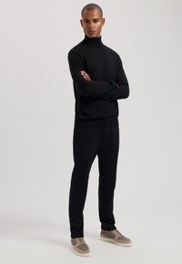 Juodas golfo megztinis ir derančios kelnės slim fit. Apranga pasižymi lygiu paviršiumi ir yra derinama su pilkais ir smėliniais sportbačiais.