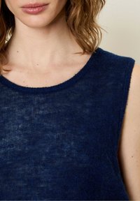 Granatowy bezrękawnik wykonany z miękkiego, teksturowanego materiału, z okrągłym dekoltem i subtelnym, nierównym wzorem.