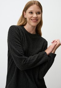 Maglione nero lavorato a maglia con texture a coste, scollatura rotonda e maniche lunghe. Il tessuto appare morbido e accogliente, con motivi sottili.