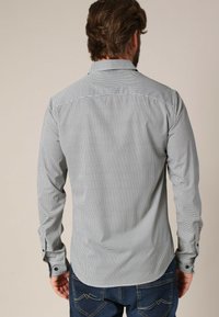 Herenoverhemd met lange mouwen, lichtgrijs met een klein zwart geblokt patroon, knoopmanchetten en een gebogen onderkant. Gemaakt van een katoenmix.