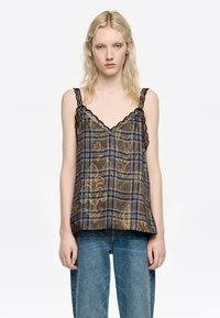 Brązowy top bez rękawów w kratę w niebiesko-żółtych odcieniach, z koronkowym wykończeniem dekoltu i dołu. Noszony z niebieskimi dżinsami.
