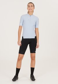 Lichtblauw fietsshirt met korte mouwen en een rits aan de voorkant, gecombineerd met zwarte fietsshorts. Ontworpen met een strakke pasvorm en een gladde textuur.