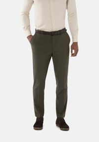 Donkergroene broek van soepel materiaal, met een getailleerde pasvorm, geplooide voorkant en zijzakken, gecombineerd met bruin schoeisel.