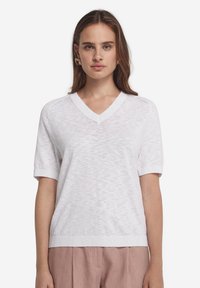 Vit stickad kortärmad tröja med V-ringning, har ett strukturerat mönster och ribbad fåll, lämplig för vardagsbruk.