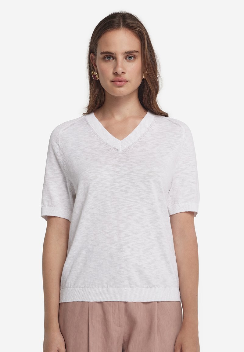 Vit stickad kortärmad tröja med V-ringning, har ett strukturerat mönster och ribbad fåll, lämplig för vardagsbruk.