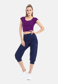 Lilla lühike topp lühikeste varrukatega, koos tumesiniste capri pükstega, millel on elastne vöökoht ja keeratud hemmed. Valged spordijalatsid täiustavad välimust.