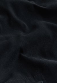 Primo piano di tessuto nero morbido con trama visibile e pieghe morbide che creano ombre uniformi.
