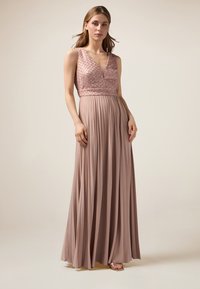Langes, plissiertes Kleid in sanftem Blush mit tiefem V-Ausschnitt und verziertem Oberteil. Glatter, fließender Stoff mit schimmernden Akzenten.
