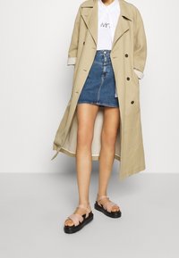 Béžový trenčkot přes bílou košili, doplněný džínovou sukní. Světle růžové sandály na černé platformě. Hladká tkanina a čisté linie.