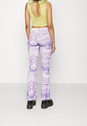 Woman wearing a lime green sleeveless top with open back and purple marble-patterned flared pants and black platform boots.