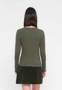 Haut à manches longues olive en tissu doux, associé à une jupe courte olive, présentant un ourlet droit et des manches longues.