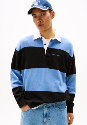 T-shirt de rugby à manches longues avec des rayures horizontales noires et bleu clair, col blanc, arbore le logo "TOMMY JEANS" sur la poitrine. Assorti à un jean clair.
