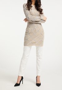 Beige stickad klänning med ett diamantmönster i silver och blått. Kombinerad med vita smala byxor och svarta spetsiga klackar.