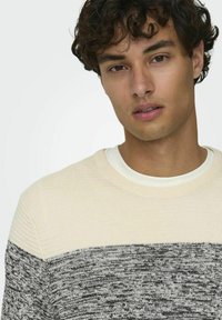 Maglione a maglia con una parte superiore color crema e una parte inferiore grigia a trama. Collo a coste e colletto interno a contrasto.