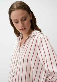 Camicia bianca con bottoni, a righe verticali rosse, con colletto e maniche lunghe, realizzata in un tessuto leggero e liscio.