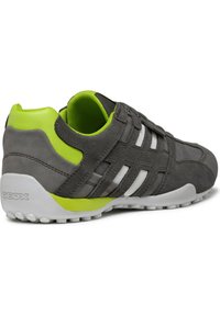 Scarpa sportiva grigia realizzata in materiali scamosciati e in mesh, con dettagli bianchi, tallone verde e suola in gomma bianca texturizzata. Marchio Geox sul tallone.