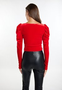 Top din catifea roșie cu mâneci lungi și umeri bufanți; asortat cu pantaloni din piele neagră, mulați; textură netedă; design simplu.