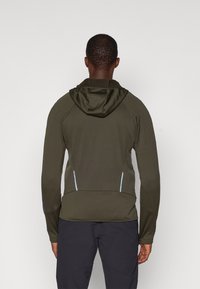 Ελαιοπράσινο μπουφάν με φερμουάρ, διαθέτει κουκούλα, ριμπ κολλάρο και μπλε λεπτομέρειες στις πλάγιες τσ pockets. Υφασμάτινη υφή με εφαρμοστό σχέδιο.