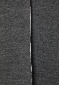 Grauer Strickstoff mit glatter Textur und einer Naht entlang einer Kante. Das Material wirkt weich und gleichmäßig in der Farbe.