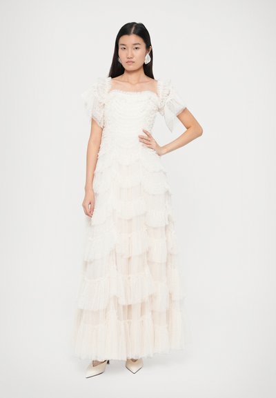 Bílé šaty se stupňovitým střihem, zdobené volánky a krátkými objemnými rukávy. Vyrobeny z lehkého materiálu, mají čtvercový výstřih a volný siluetu.