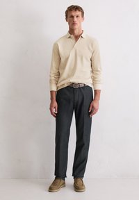 Beige Langarm-Polohemd mit Kragen, kombiniert mit dunkelgrauen Hosen und hellbraunen Wildlederschuhen. Einfaches Design, keine Muster oder Akzente.