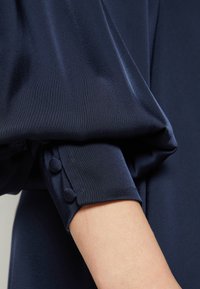 Navy dress fabric with a smooth texture and gathered sleeves. Cuff features three matching, fabric-covered buttons for detail.