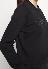 Svart sweatshirt med rund halsringning, långa ärmar och en texturerad "BOSS"-detalj på framsidan. Mjuk tygkvalitet och figurnära passform.