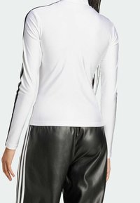 Vit långärmad tröja med hög krage, prydd med svarta sidostreck; kombinerad med svarta byxor i konstläder, som visar en slät yta.