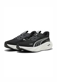 Scarpe da ginnastica nere con tomaia in maglia testurizzata, suola bianca e dettagli riflettenti. Dispongono di un'ammortizzazione intermedia e di un sistema di allacciatura tradizionale.