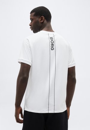 Fehér, rövid ujjú ingben álló férfi, amelyen függőleges fekete csíkok és a "BORG" felirat látható a hátoldalon, egyszínű fehér háttér előtt.