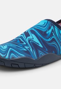 Blå och marinblå slip-on sko med ett marmorerat mönster, utrustad med en flexibel sula och en strukturerad textilöverdel.