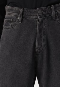 Blugi din denim negru cu un finisaj texturat, având cinci buzunare, bucle pentru curea, închidere cu buton și cusături în contrast.